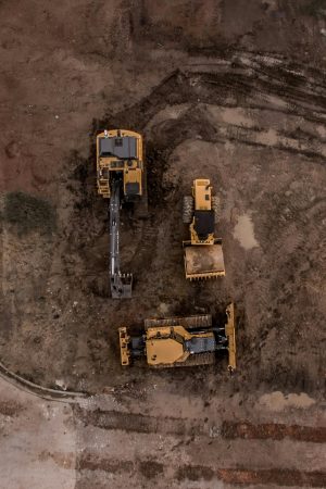 An aerial shot of heavy machinery at a construction site, including excavators and road rollers.