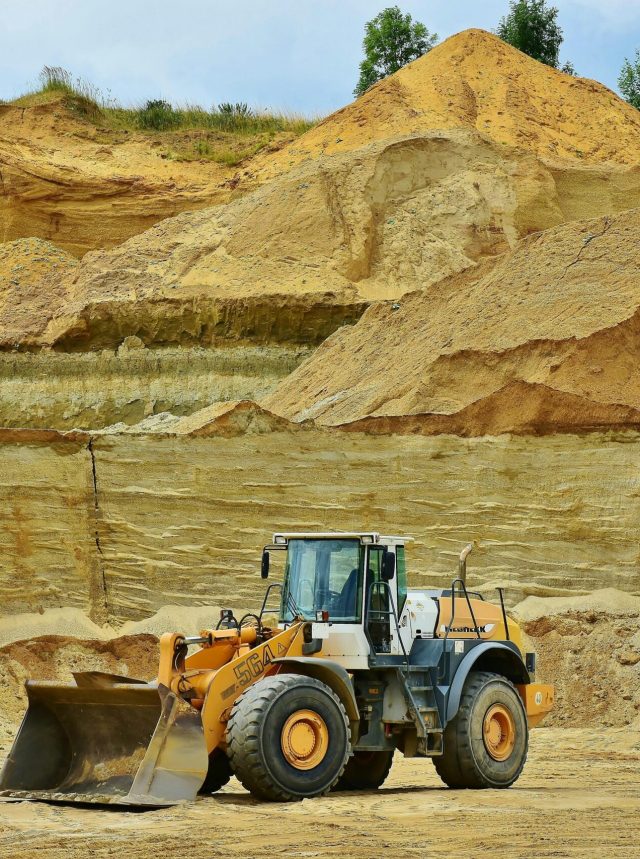 An excavator working in an open pit mine surrounded by sandy terrain and clear sky.